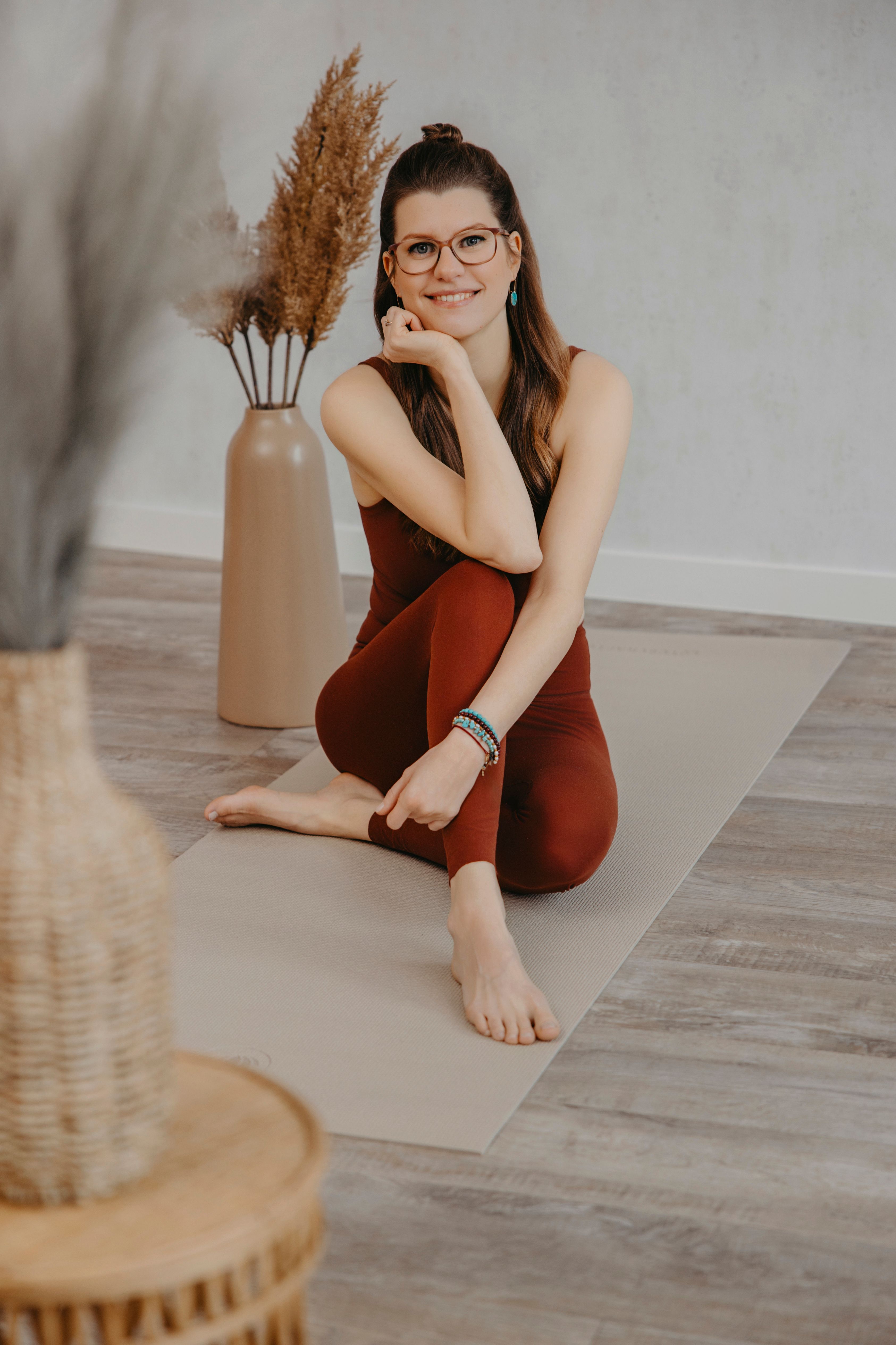 Yoga-Lehrerin Sharon sitzt lächelnd mit übergreuzten Beinen auf einer Yoga Matte in einem Studio.